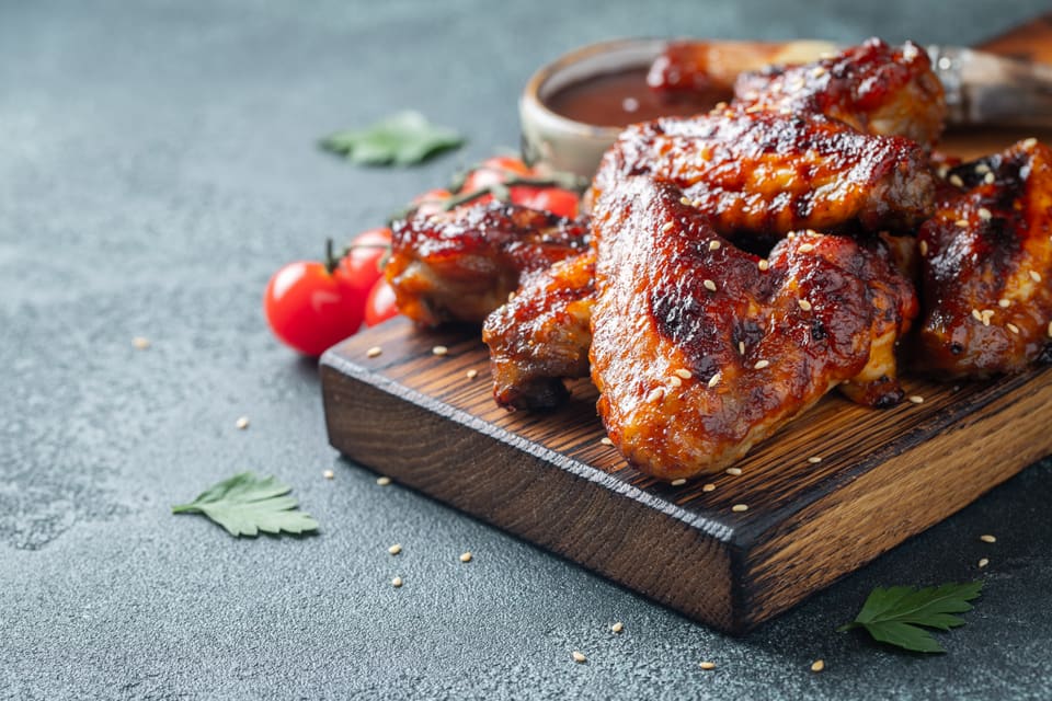 Gljáðir grillaðir kjúklingavængir á bretti með ídýfu.