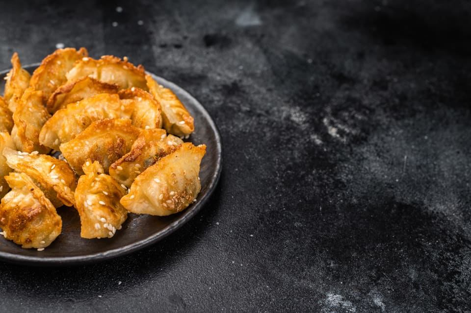 Stökk steikt dumplings með sesamfræjum á dökkum diski.