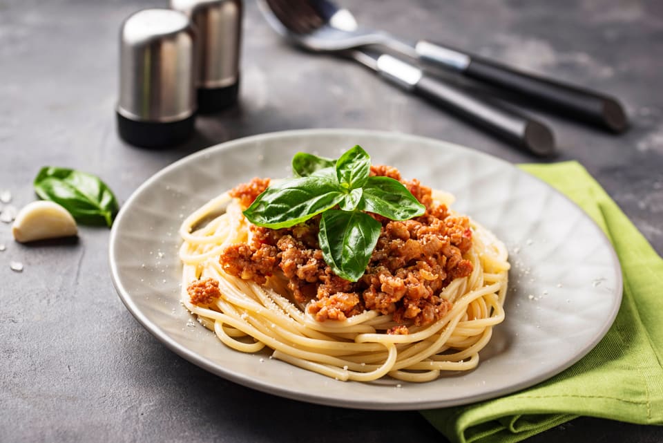Spaghetti með nautahakkssósu og basilíku á gráum diski.