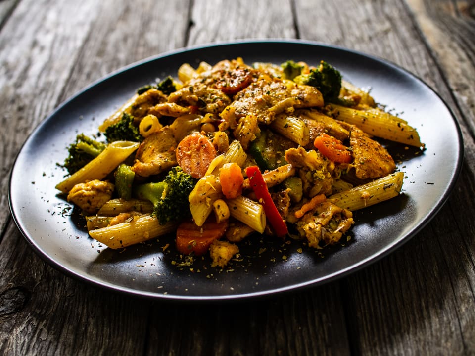 Steikt pasta með kjúklingi, spergilkáli og papriku á svörtum diski.